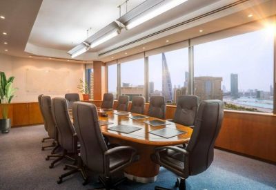 Spacious boardroom with a large oval wooden table and panoramic city skyline views through floor-to-ceiling windows.