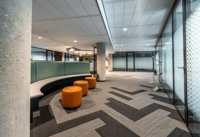 Modern communal lounge area with orange ottomans, a curved bench, and patterned grey carpet.