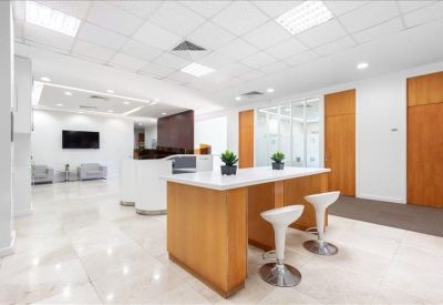 Sleek coworking lounge area with wooden central tables and stylish white bar stools.