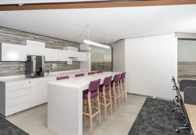 Modern communal kitchen and breakout area with white cabinetry and a long breakfast bar with purple stools.