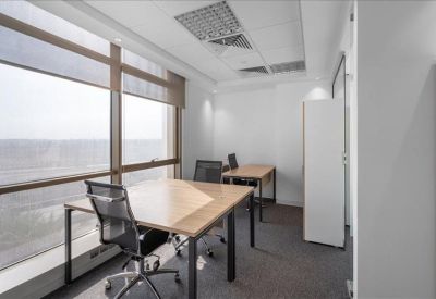 Bright corner office with two wooden desks and expansive city views through large windows.