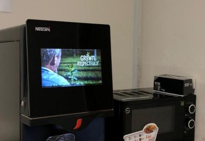 Office kitchen area featuring a coffee machine and microwave on a wooden shelf.