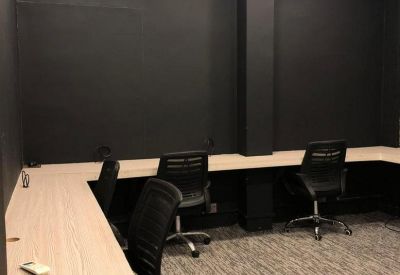 Clean, minimalist workstation area with light wood desks and black ergonomic chairs against dark walls.
