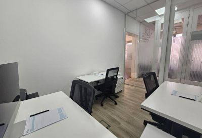 Bright shared workspace with white desks and black mesh chairs.