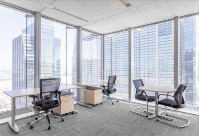 Spacious corner office with three desks and floor-to-ceiling windows overlooking skyscrapers.