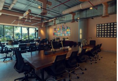 Spacious workspace with long tables and chairs under industrial ceiling.