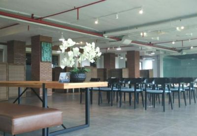 Spacious coworking area with wooden tables, black chairs, and white orchid centerpieces.