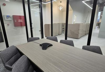 Modern conference room with a long wood-grain table and grey fabric chairs behind glass partitions.