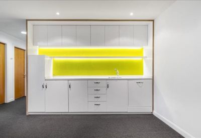 Minimalist white kitchen area featuring a bright yellow splashback.