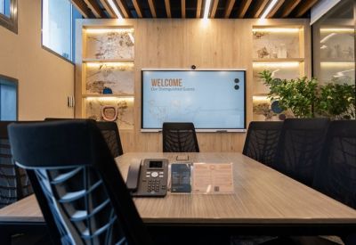 Modern meeting room with large video conferencing screen, wooden table, and plant life.
