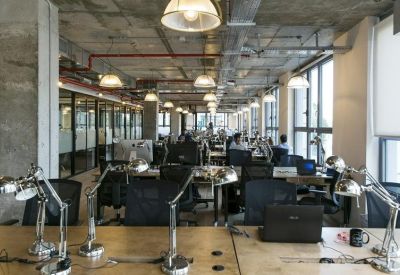 Open-plan office with rows of desks, task lamps, and high industrial ceilings.
