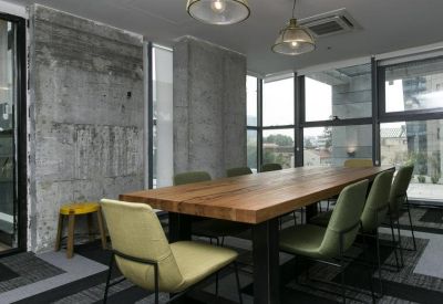 Industrial-style meeting room with a long wood table, green chairs, and concrete walls.