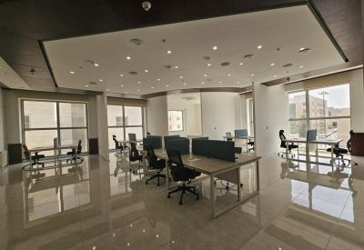 Spacious open-plan workspace with multiple desks, ergonomic chairs, and large windows.
