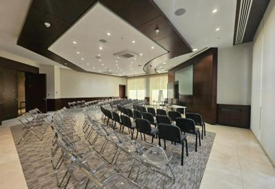 Lecture-style meeting room with rows of black chairs and a presentation screen.