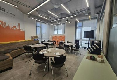 Bright communal dining area with round tables and a city skyline mural.