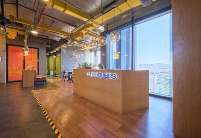 Wooden reception desk in a sunlit lobby with large windows and city views.