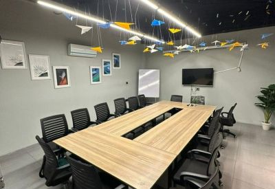 Large meeting room with a wooden U-shaped table, black ergonomic chairs, and colorful paper plane art.