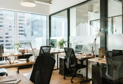 Modern open-plan office space with black ergonomic chairs and large windows.