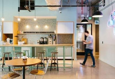 Bright kitchen and breakout area with high stools and a neon wall sign.