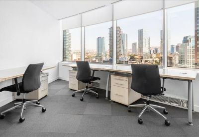 Bright three-person workspace with long desks and expansive city views through floor-to-ceiling windows.
