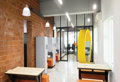 Open-plan coworking space with a brick feature wall, orange benches, and a yellow circular pod.