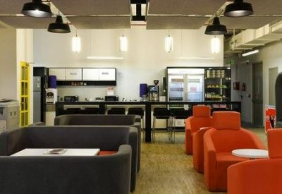 Vibrant breakout area featuring orange armchairs, grey sofas, and a kitchenette.
