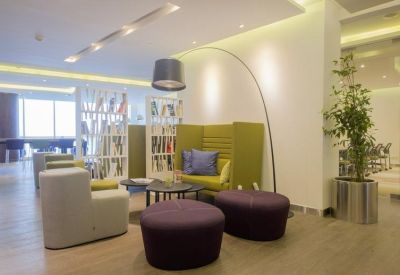 Vibrant lounge area with purple ottomans, a green high-back sofa, and a large arched lamp.