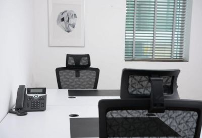 Private office suite featuring a white desk, telephone, and grey mesh chairs by a window.