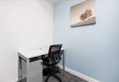 Bright shared office space with white desks, privacy screens, and ergonomic black chairs.
