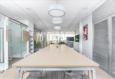 Long communal coworking table under circular pendant lights in a bright, modern corridor.