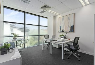 Spacious sunlit office with two workstations and floor-to-ceiling windows.