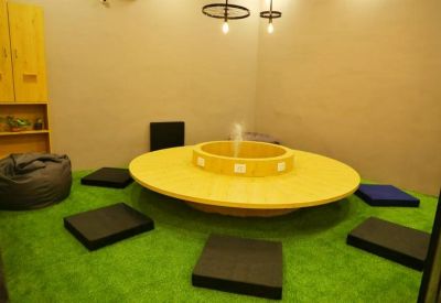 Creative breakout area with a central circular yellow table, bean bag, and artificial grass flooring.