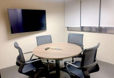 Small meeting room with a round wooden table, four black chairs, and a wall-mounted TV.