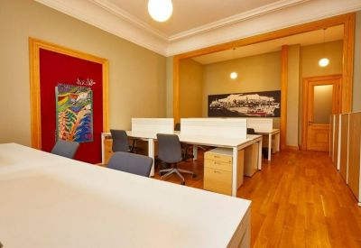 Open-plan office with white desks, grey chairs, and a red feature wall with artwork.