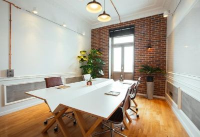 Bright workspace featuring a white double-sided desk, modern pendant lights, and indoor plants.