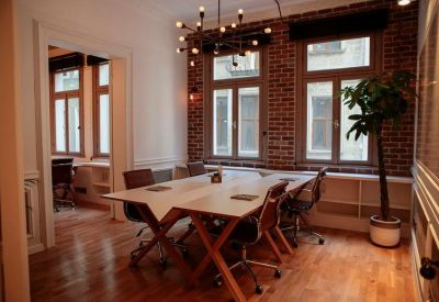 Symmetric office space with white tables, an industrial chandelier, and large windows.