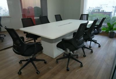 Bright conference room with a large white table, ergonomic black chairs, and wooden flooring.
