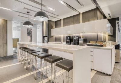 Sleek office kitchen and break area with a long white breakfast bar and modern black stools.
