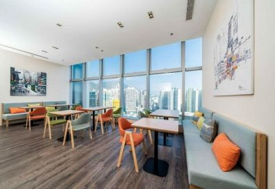 Spacious communal lounge with diverse seating, colourful cushions, and expansive city views through floor-to-ceiling windows.