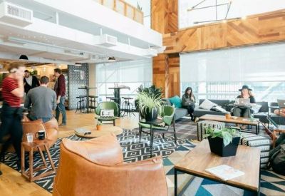 Modern coworking space featuring wooden wall accents, leather armchairs, and people working at tables.