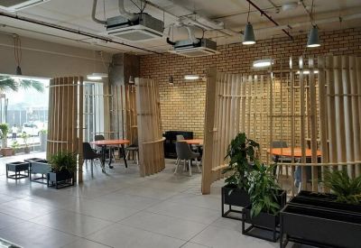 Open-plan coworking space with wooden privacy screens, orange tables, and various seating pods.