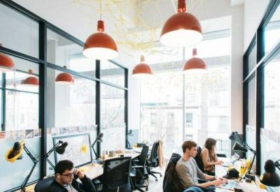 Bright open-plan workspace with glass partitions and orange pendant lights over rows of desks.