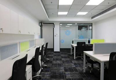 Open-plan workspace with rows of white desks and black ergonomic chairs.
