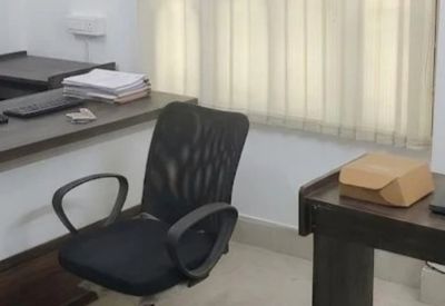 Workstation area with an ergonomic black chair, desk, and vertical window blinds.