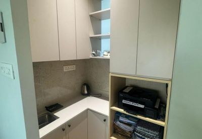 Compact office kitchenette area featuring white cabinetry, wood-style flooring, and open shelving for supplies.