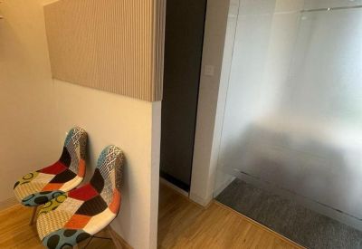 Waiting area featuring two vibrant patchwork upholstered chairs against a clean white wall and wooden floor.