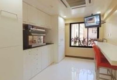 Sleek office kitchen and break area with white cabinetry and a breakfast bar with red stools.
