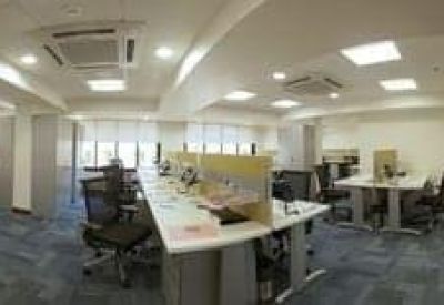 Modern open-plan office space featuring rows of desks with ergonomic chairs and bright overhead lighting.