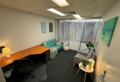 Small office featuring a teal sofa, wooden corner desk, and framed wall art.