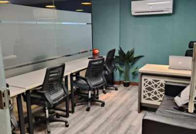 Long white desks with black office chairs against a teal feature wall.